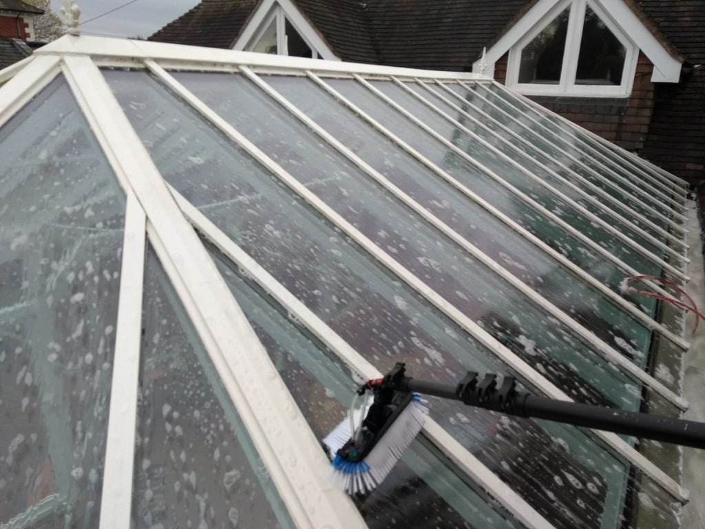 Cleaning a conservatory roof with a window cleaning brush and a mild detergent to loosen up the dirt