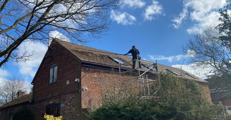 Scraping the moss off a slate roof to clean it and improve aesthetics. The worker is stood on a scaffold access tower for safety and using a special scraper blade and a telescopic pole