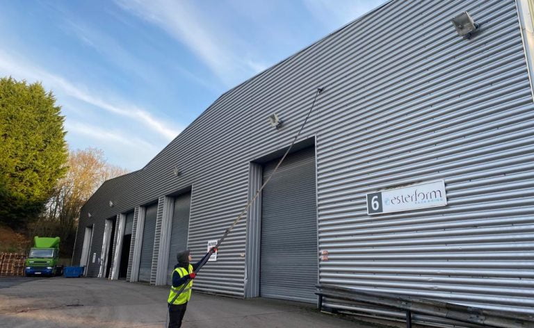 Cleaning commercial metal cladding on a large factory unit from the ground with a water fed window cleaning pole and hot water