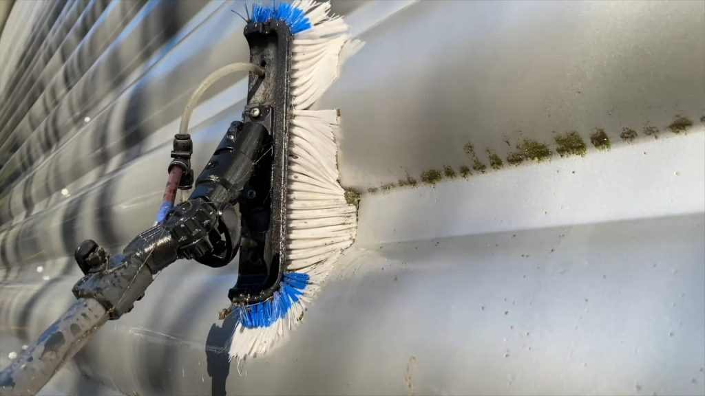 Cleaning cladding on a factory unit with a water fed brush